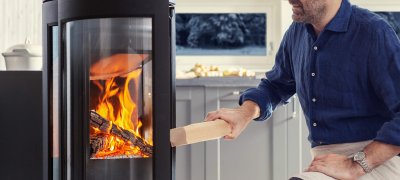 Jøtul F 373 Advance wood stove in black cast iron with a man adding wood