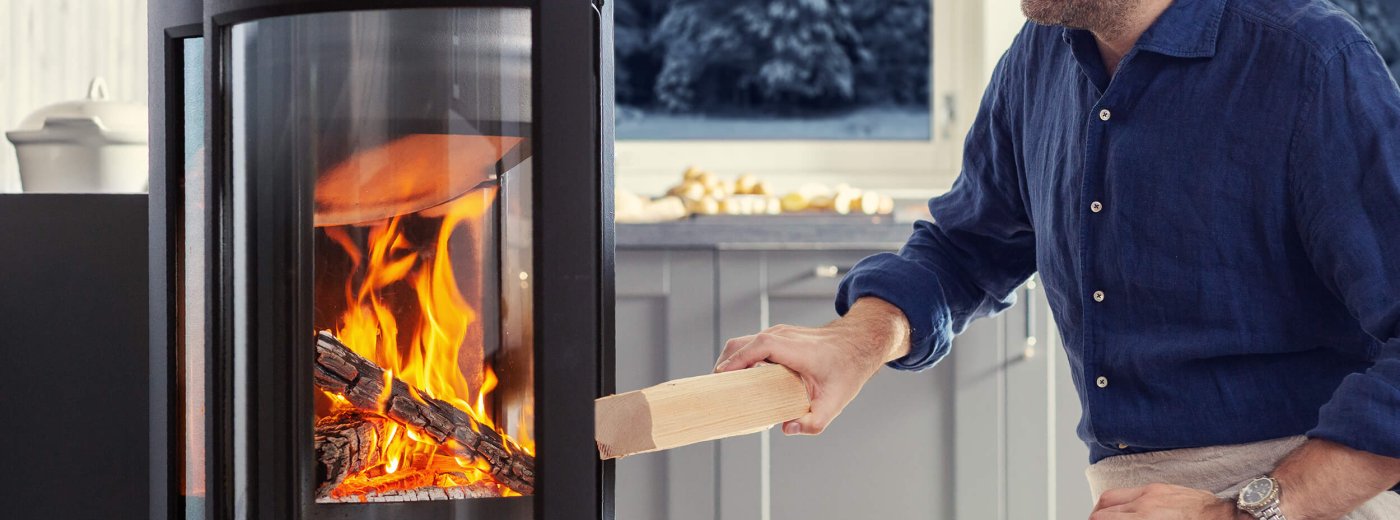 Jøtul F 373 Advance wood stove in black cast iron with a man adding wood